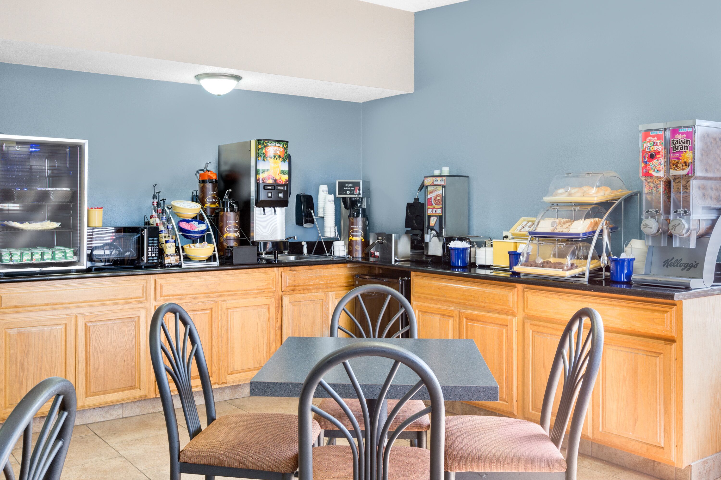 A kitchen area with a dining table, chairs, a microwave, coffee maker, and various food items.