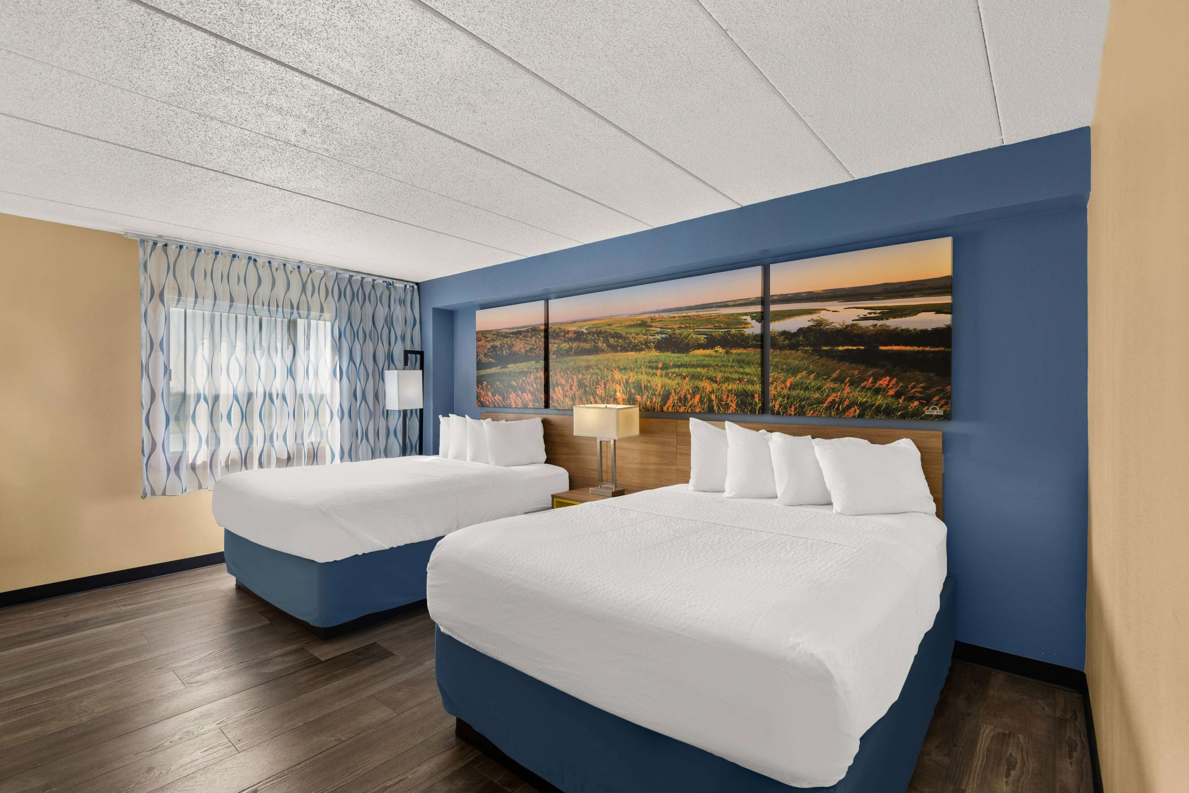 A hotel room with two beds, a large window with a landscape view, and a patterned curtain.