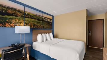 Habitación de hotel con cama, escritorio con lámpara, teléfono y un cuadro de un paisaje en la pared.