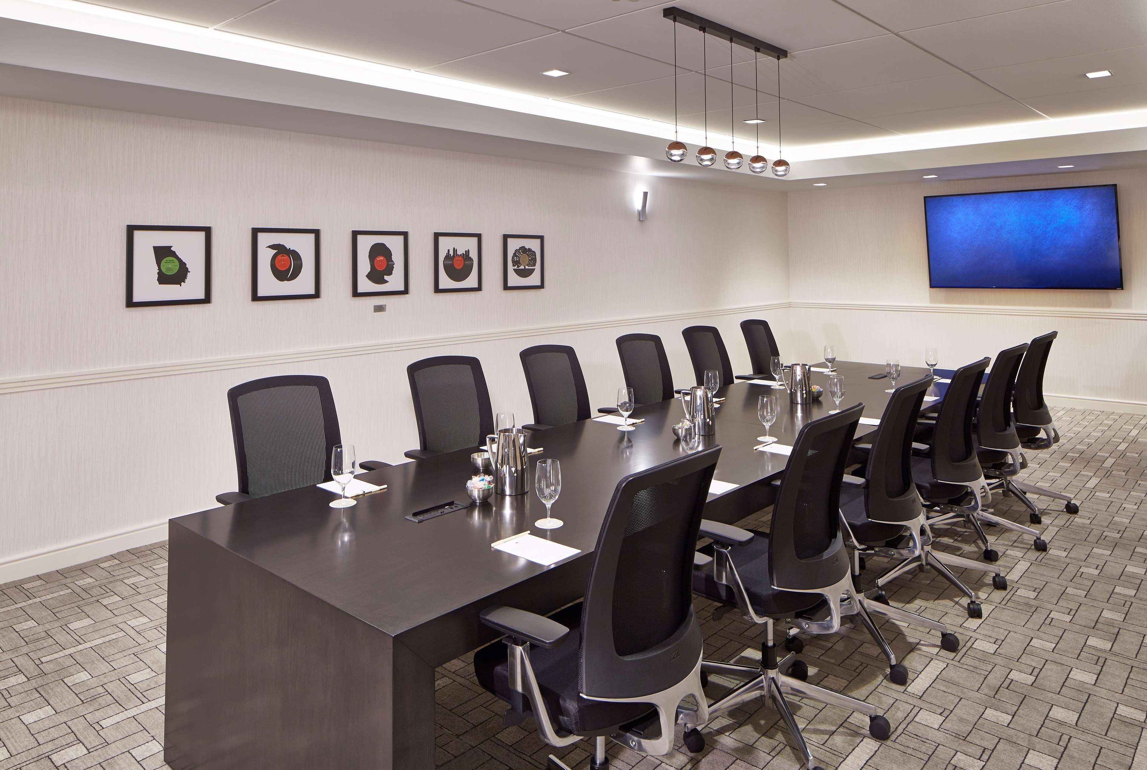 A conference room with a long table, chairs, a flat-screen TV, and framed artwork on the wall.