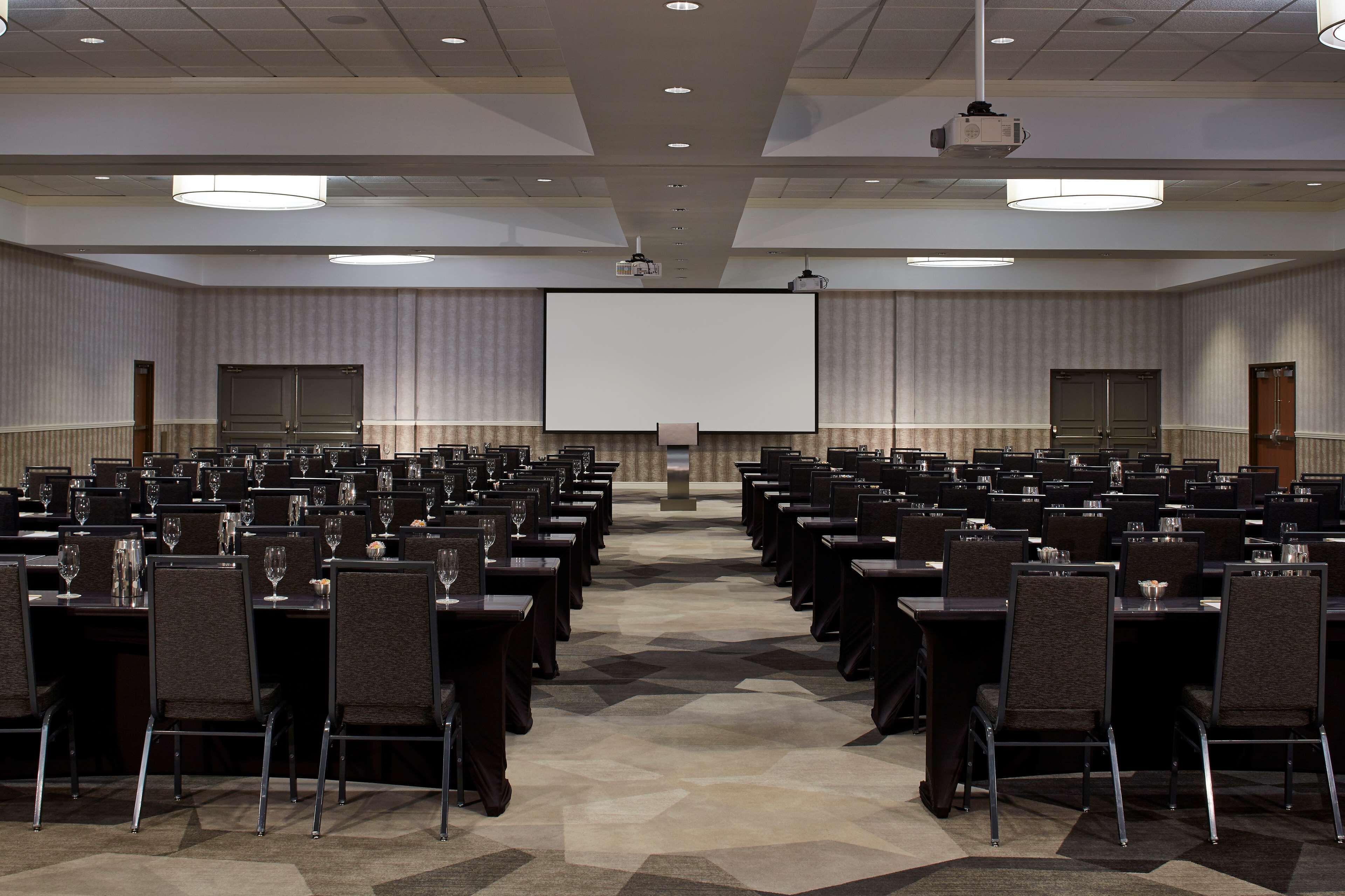 A conference room with rows of tables and chairs, a large screen at the front, and a projector mounted on the ceiling.