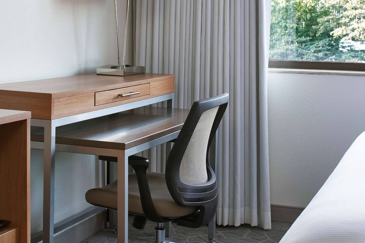 A hotel room with a desk, chair, lamp, and bed.