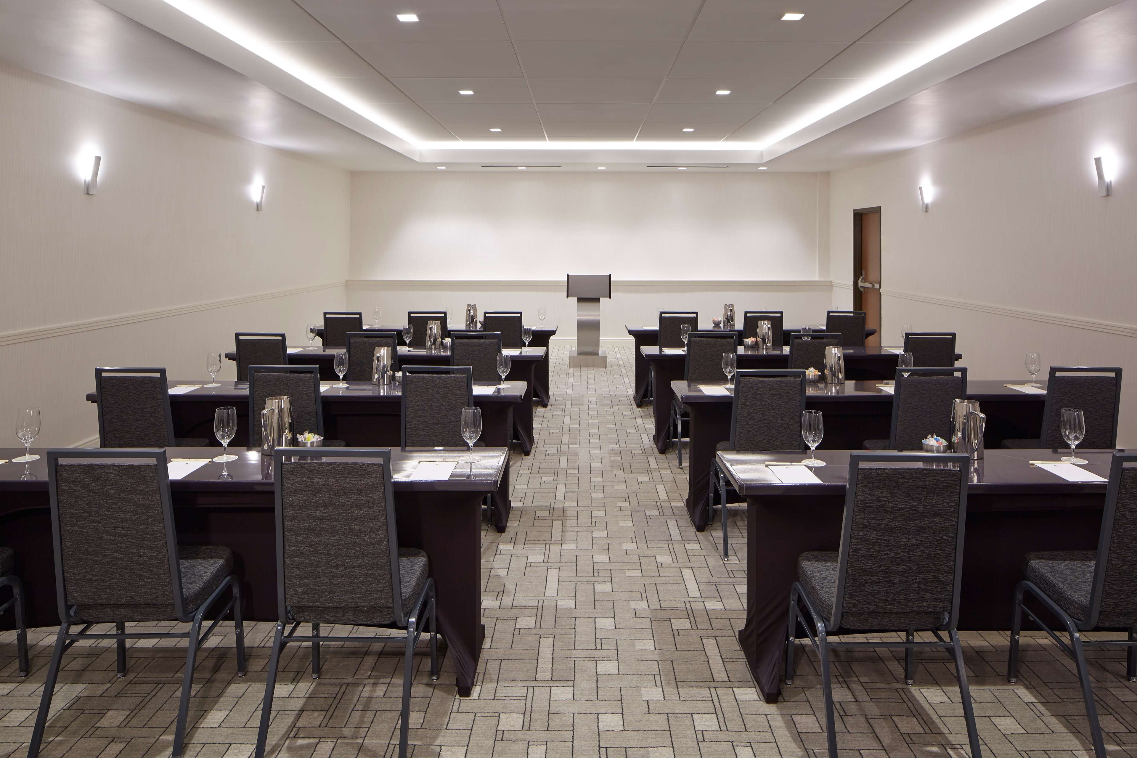 Un salón de conferencias con varias mesas y sillas, equipado con copas de vino y botellas de agua.