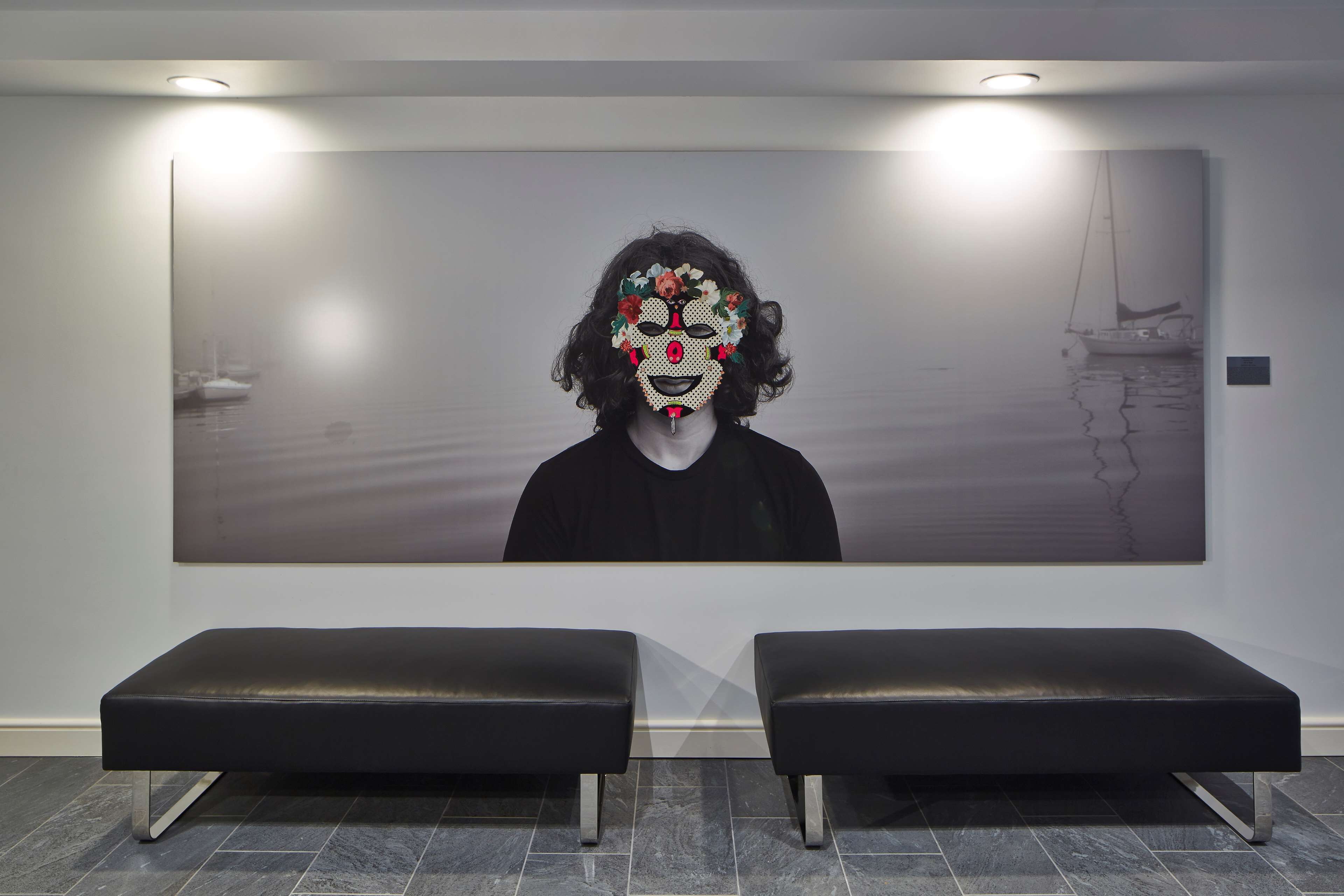 A reception area with a large wall-mounted artwork, two black benches, and a tiled floor.