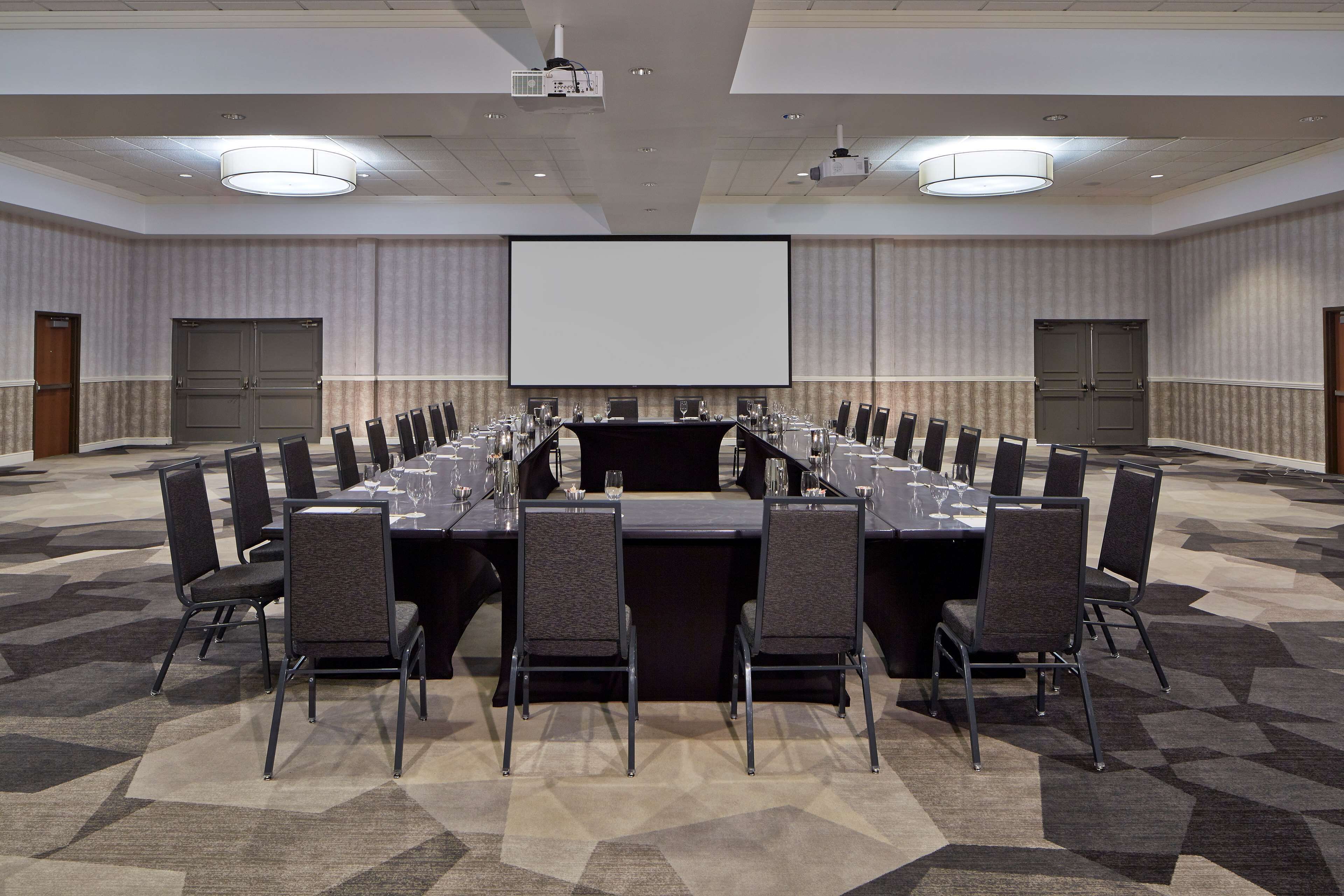 A conference room with a long table, chairs, a projector screen, and a carpeted floor.