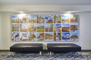 A wall with a large, colorful cityscape artwork. There are two black leather benches in front of the artwork.