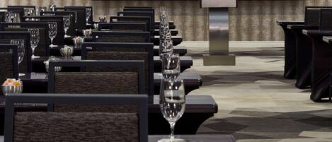 A conference room with rows of tables, each with a wine glass, and a large screen at the front.