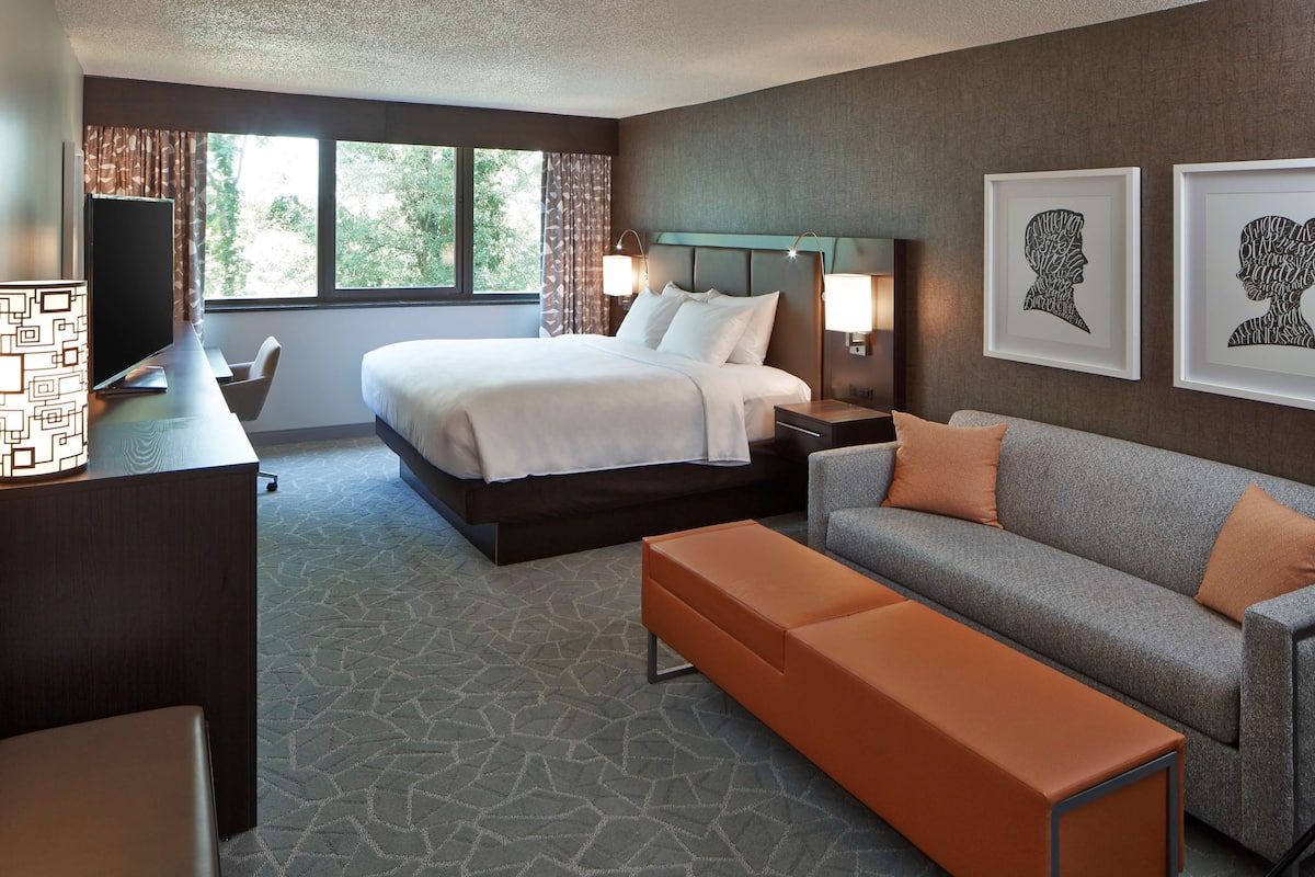A hotel room with a bed, a sofa, a bench, a desk with a lamp, and two wall-mounted lamps.