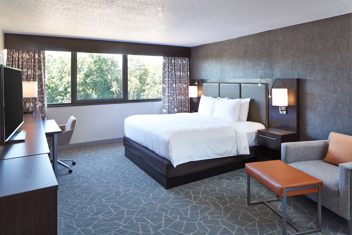 A hotel room with a bed, a desk, a chair, a TV, and a window with curtains.