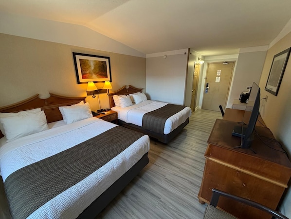 A hotel room with two beds, a desk, a chair, a TV, and a painting on the wall.