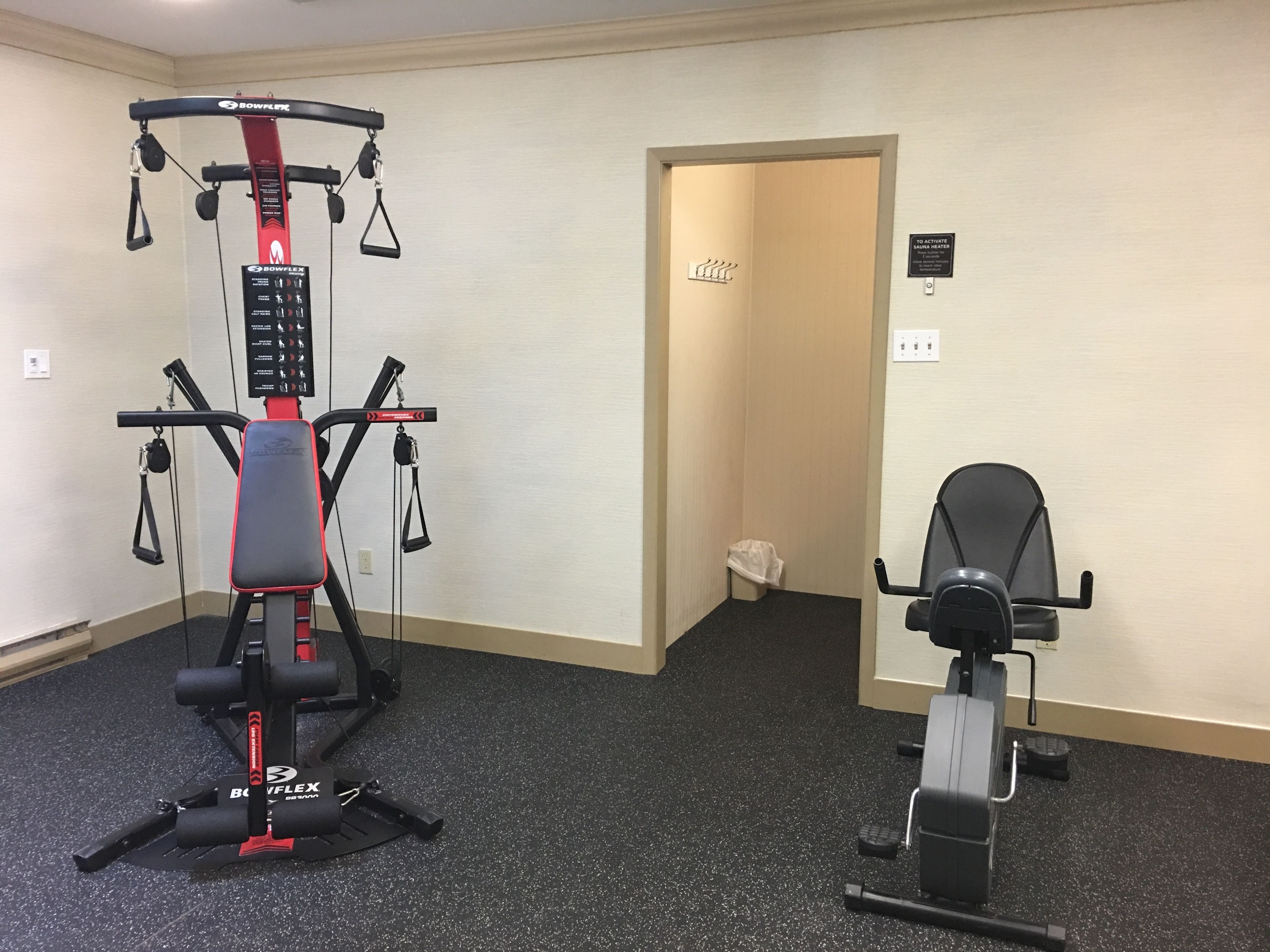 Een fitnessruimte met een Bowflex-apparaat en een elliptische trainer.