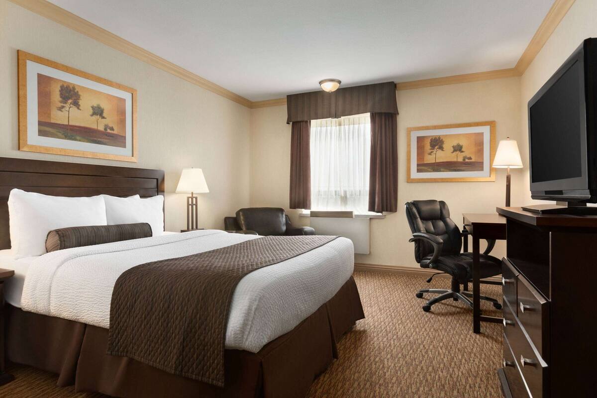 Ein Hotelzimmer mit einem großen Bett, einem Schreibtisch, einem Sessel, einem Fernseher und zwei gerahmten Bildern an der Wand.