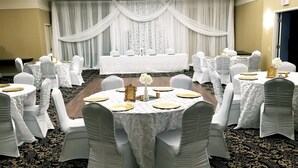 A banquet hall with round tables, white tablecloths, and chairs with white coverings. - Days Inn & Suites by Wyndham Sault Ste. Marie ON (Sault Ste. Marie)