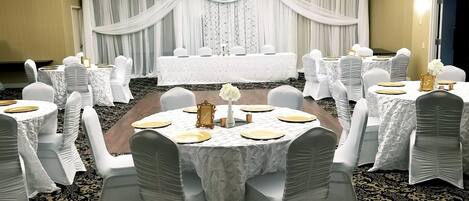 Une salle de banquet avec des tables rondes, des nappes blanches et des chaises recouvertes de housses blanches.