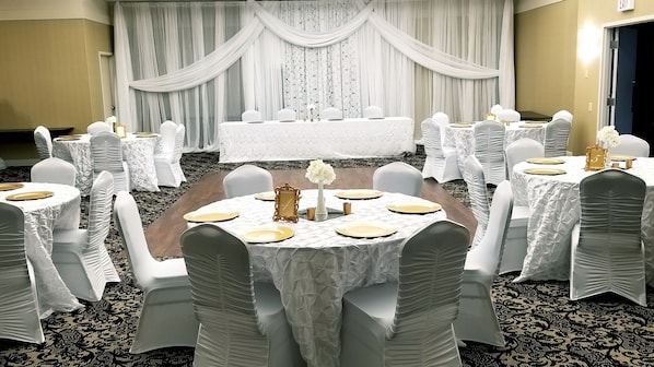 A banquet hall with round tables, white tablecloths, and chairs with white coverings.