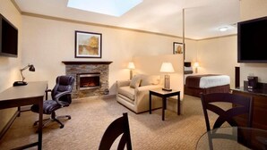 A hotel room with a fireplace, a sofa, a bed, a desk, and a TV. - Days Inn & Suites by Wyndham Sault Ste. Marie ON (Sault Ste. Marie)