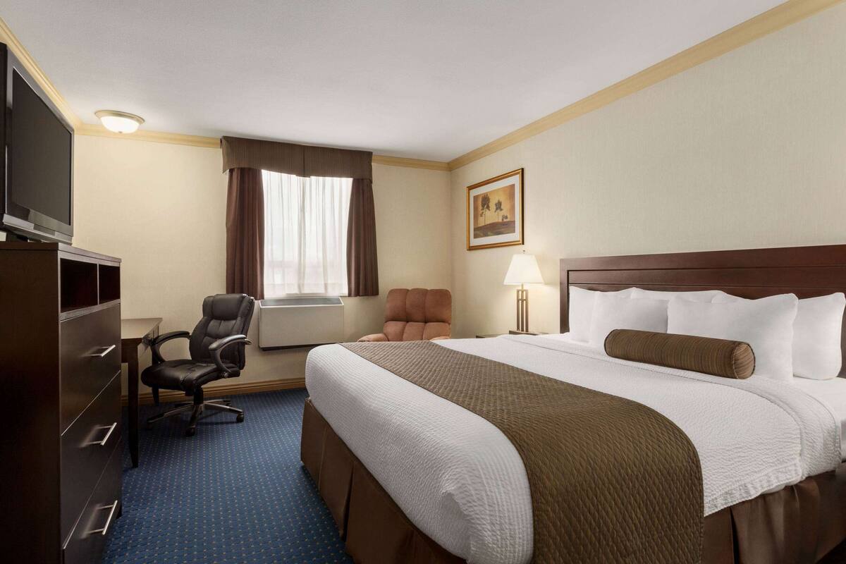 Ein Hotelzimmer mit einem großen Bett, einem Schreibtisch mit Stuhl, einem Fernseher und einem Fenster mit Vorhängen.