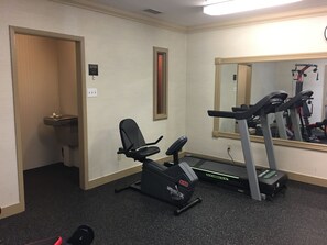 A gym with a treadmill, a stationary bike, and a bench.