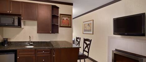 A kitchen with a microwave, cabinets, a sink, and a bar area. There is a fireplace with a TV above it.
