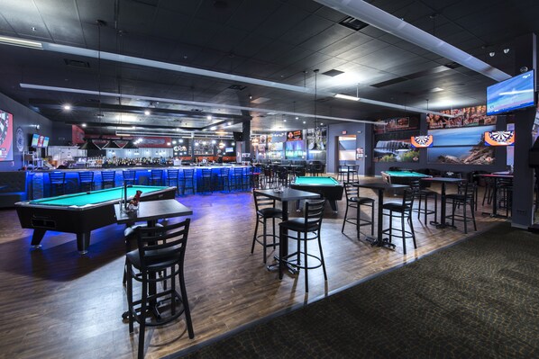 A bar area with pool tables, chairs, and a television screen.