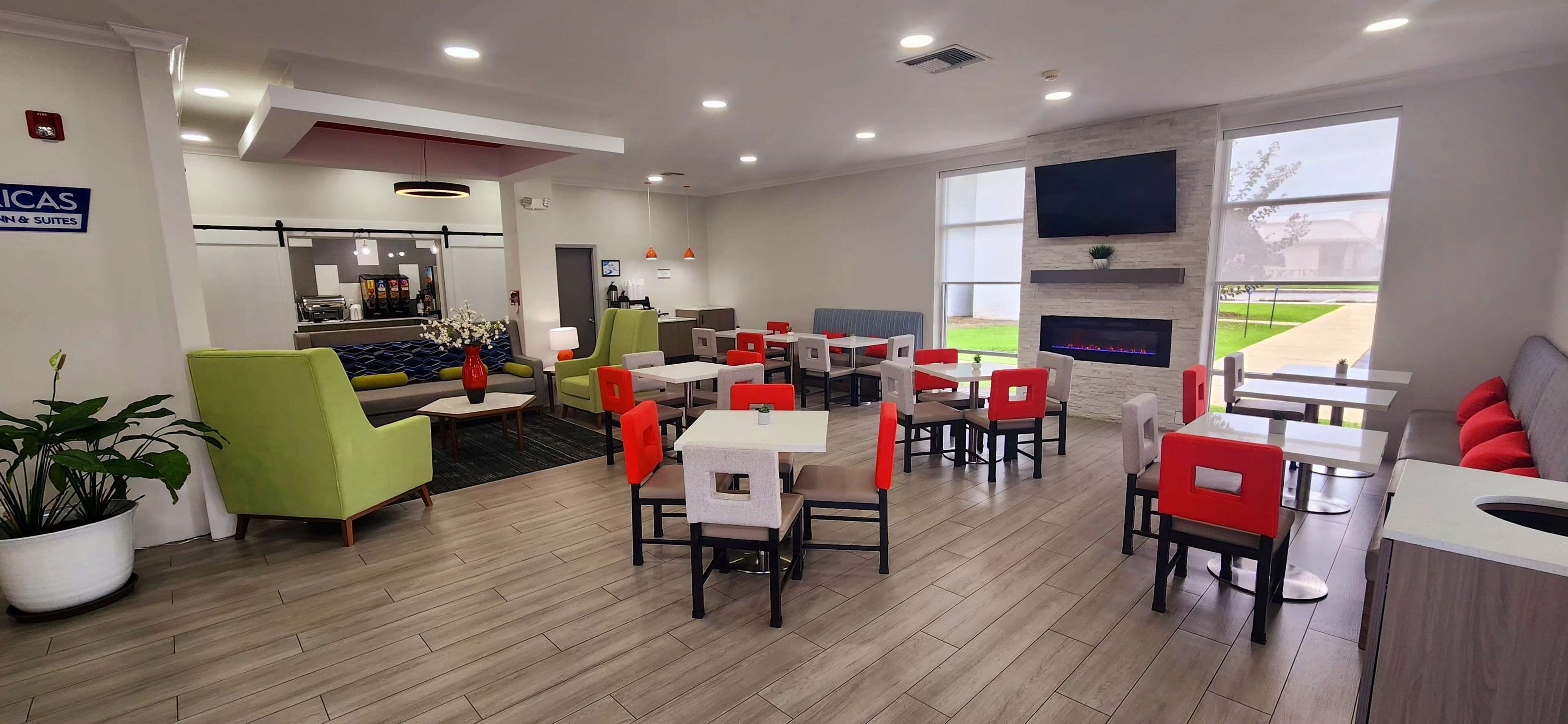 A modern restaurant with a mix of red and green chairs, a flat-screen TV mounted on the wall, and a fireplace.