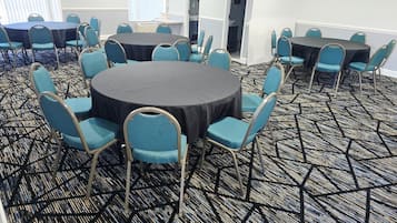 Un salón de conferencias con mesas redondas y sillas azules, piso alfombrado y un cuadro en la pared.