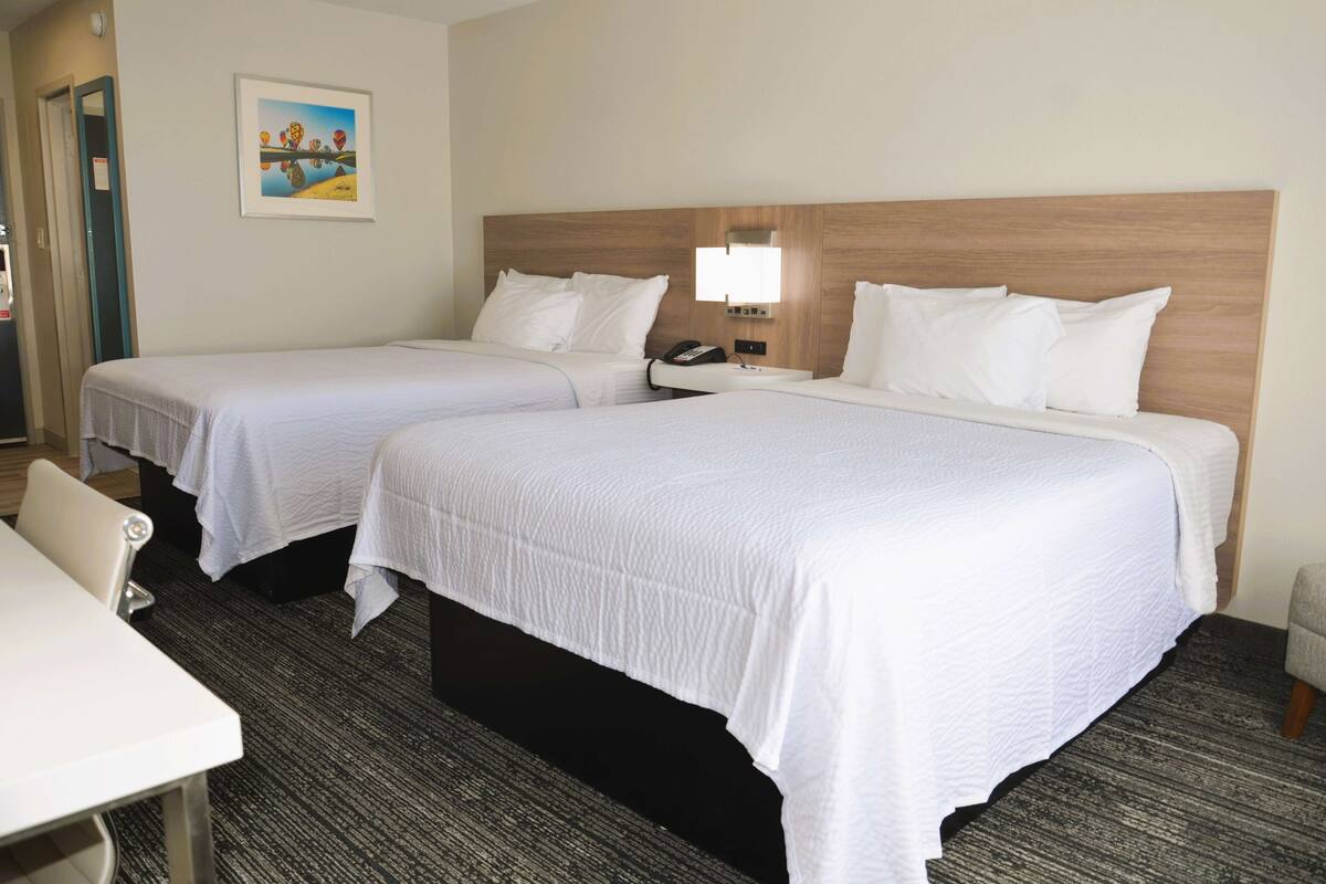 A hotel room with two beds, a desk, and a chair.