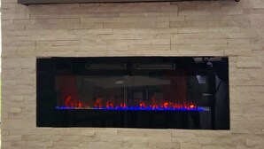 A modern living room with a flat-screen TV mounted on a brick wall, a small potted plant, and a built-in fireplace with a glass front.
