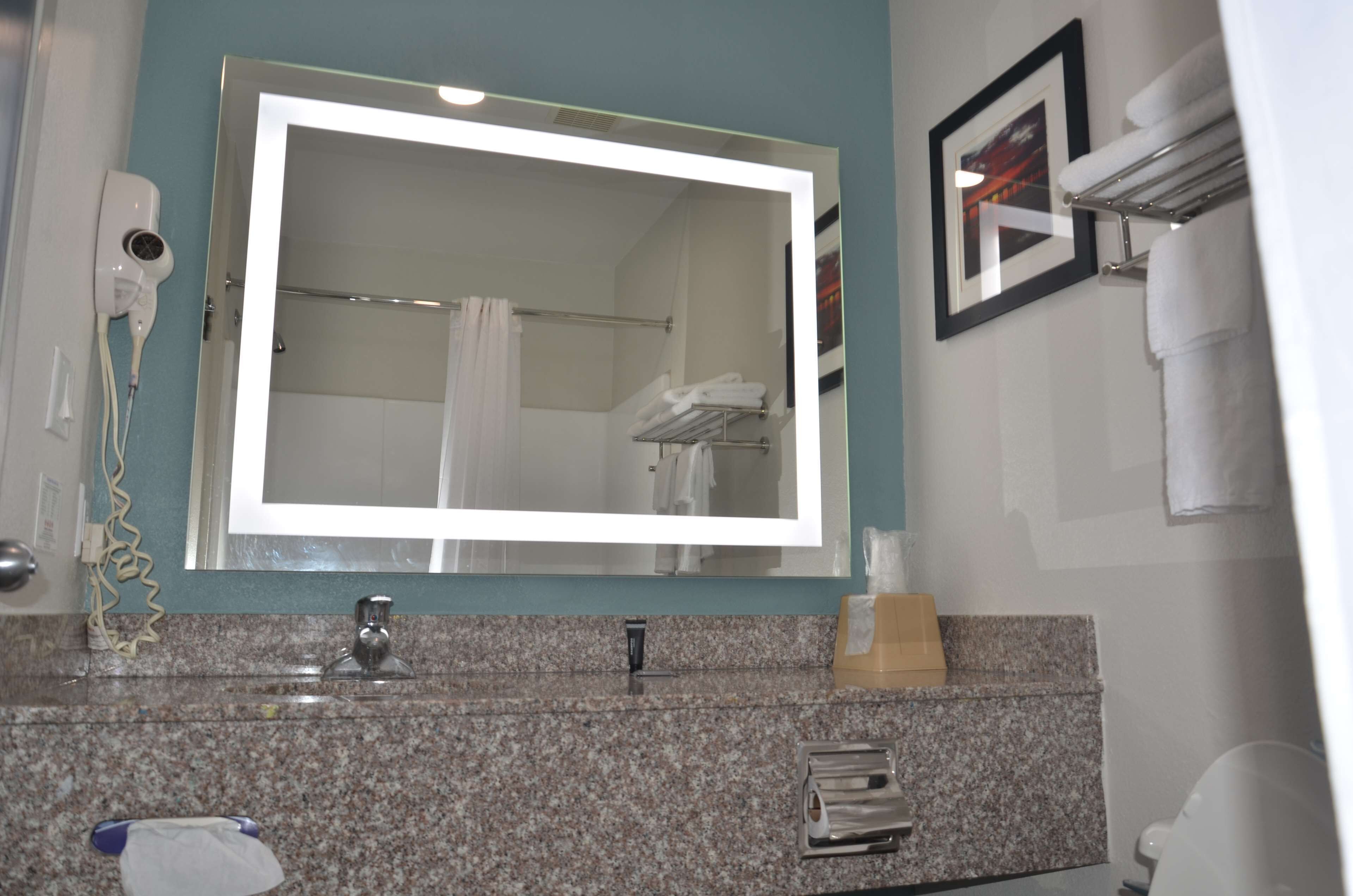A bathroom with a large mirror, a hairdryer, a towel rack, and a sink with a granite countertop.