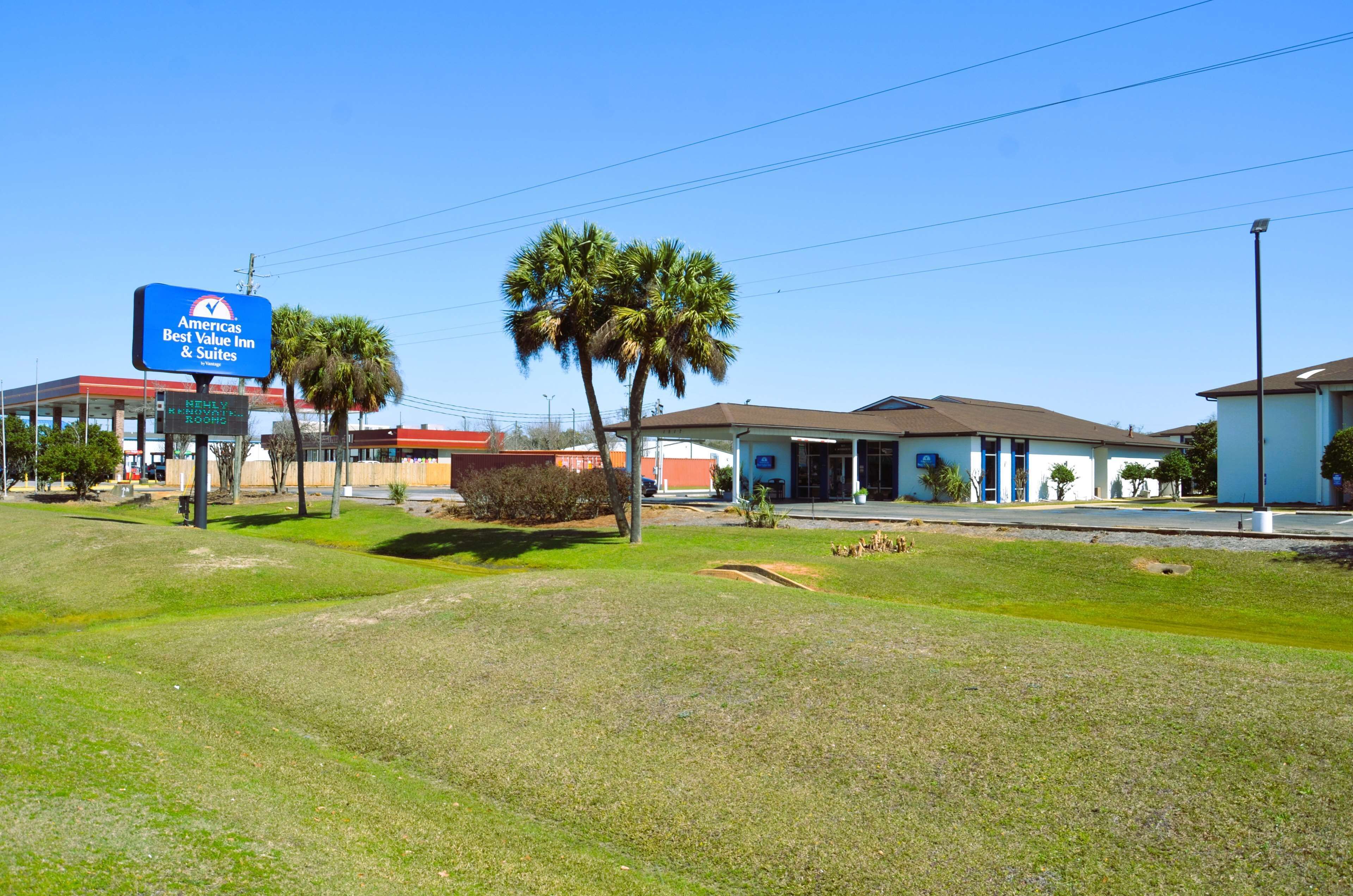 A hotel with a sign for 'Americas Best Value Inn & Suites' and a well-maintained lawn with palm trees.