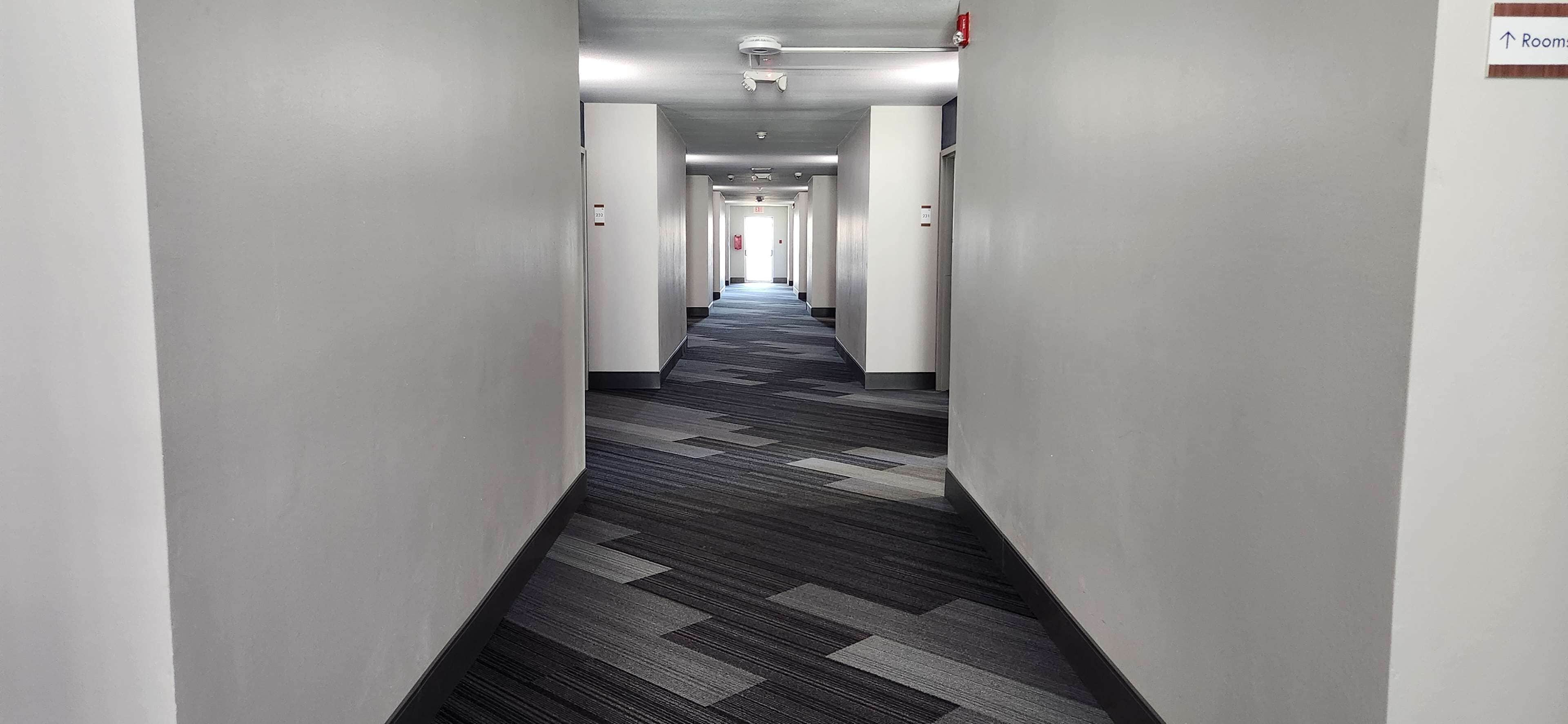 A long, narrow hotel corridor with a patterned carpet and white walls.