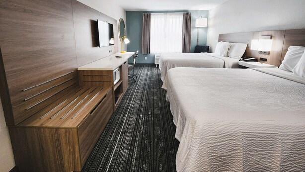 A hotel room with two beds, a desk, a mirror, a lamp, and a window with curtains.