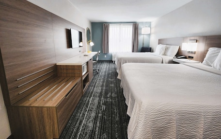 A hotel room with two beds, a desk, a mirror, a lamp, and a window with curtains.