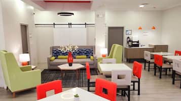A modern hotel lobby with a sofa, chairs, tables, and a coffee station.