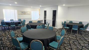 A conference room with round tables and teal chairs, carpeted floor, white walls, and a painting.