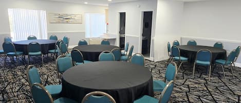 A conference room with round tables and teal chairs, carpeted floor, white walls, and a painting.