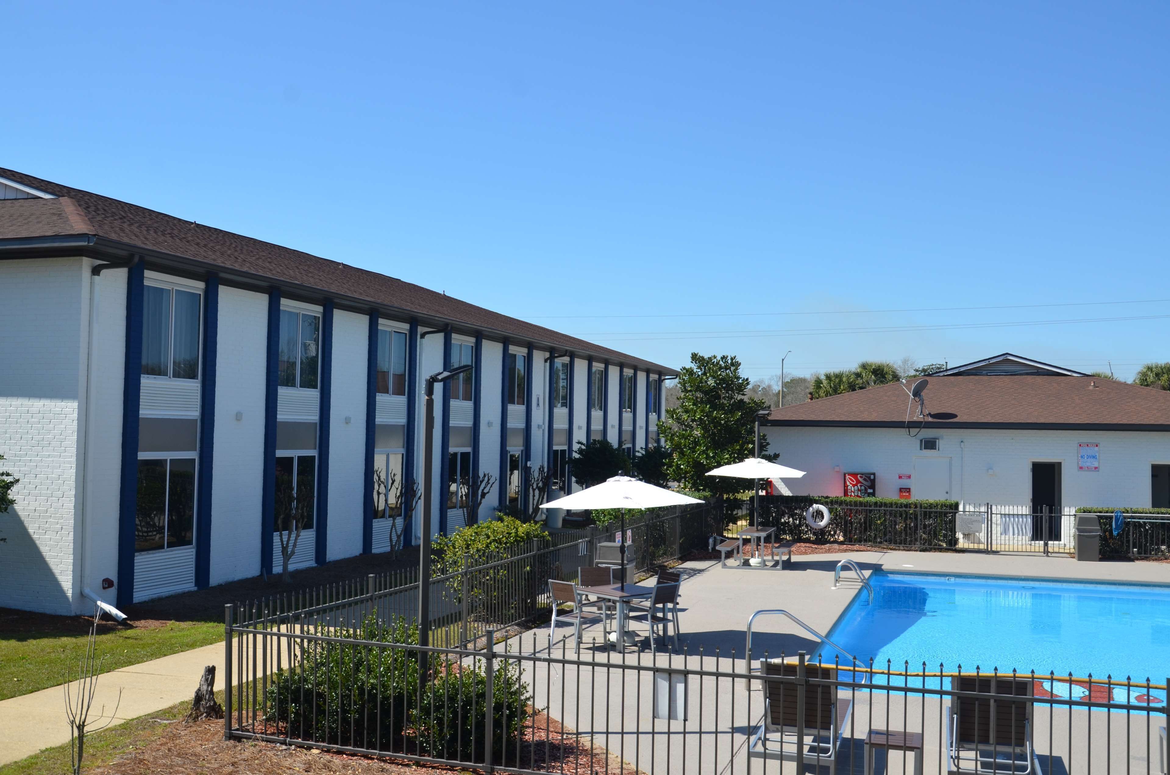 A motel with a swimming pool, outdoor seating, and a fenced patio area.