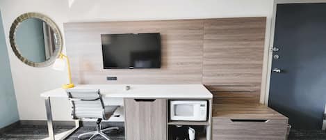 A hotel room with a desk, chair, TV, microwave, and a door.