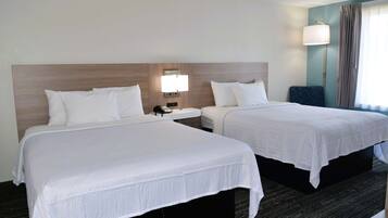 A hotel room with two beds, a nightstand with a lamp, and a view of the outdoors.