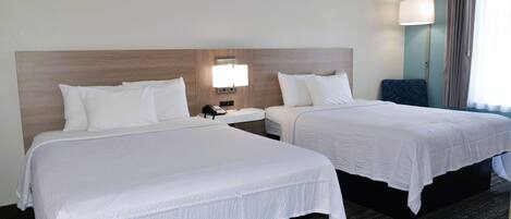 A hotel room with two beds, a nightstand with a lamp, and a view of the outdoors.