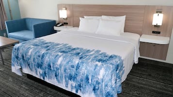 A hotel room with a large bed, a blue armchair, bedside tables with lamps, and a carpeted floor.
