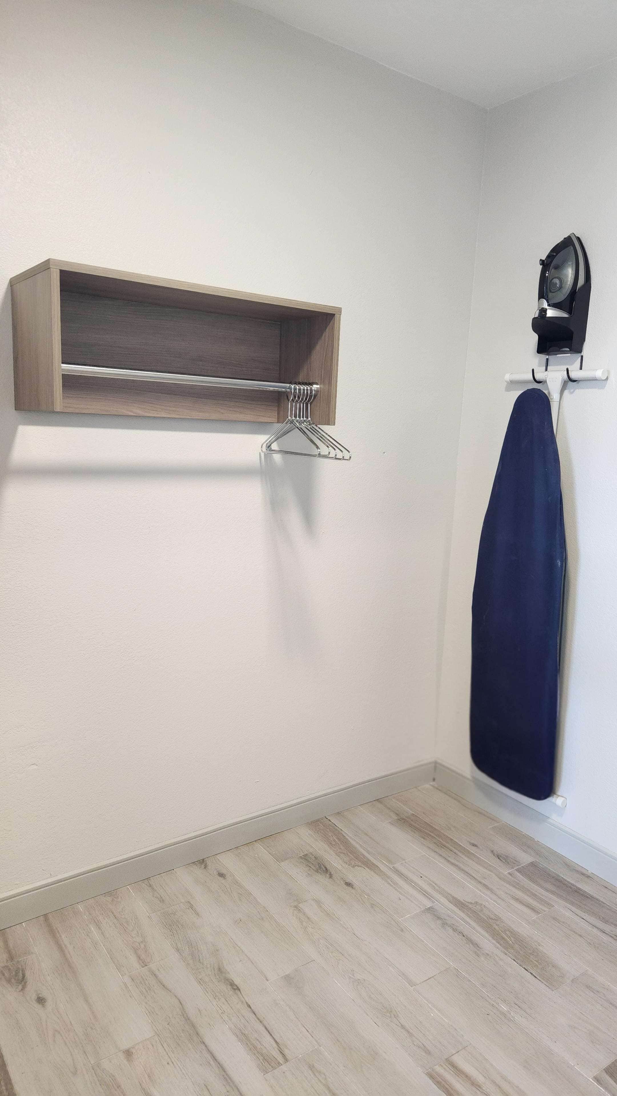 A room with a wooden shelf, a hanging clothes rack, and a steam iron.