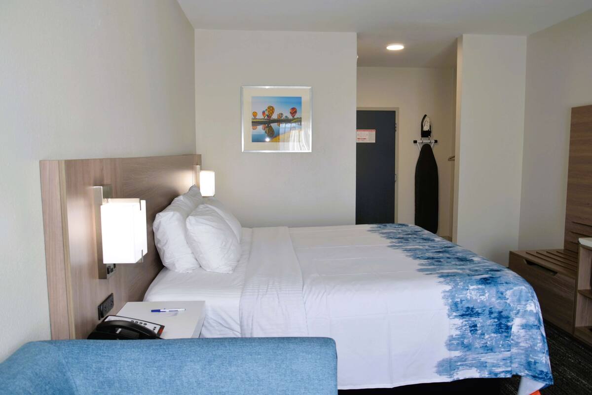 A hotel room with a bed, a desk, a chair, a painting on the wall, and a door.