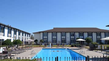 A hotel with a swimming pool, sun loungers, and umbrellas.