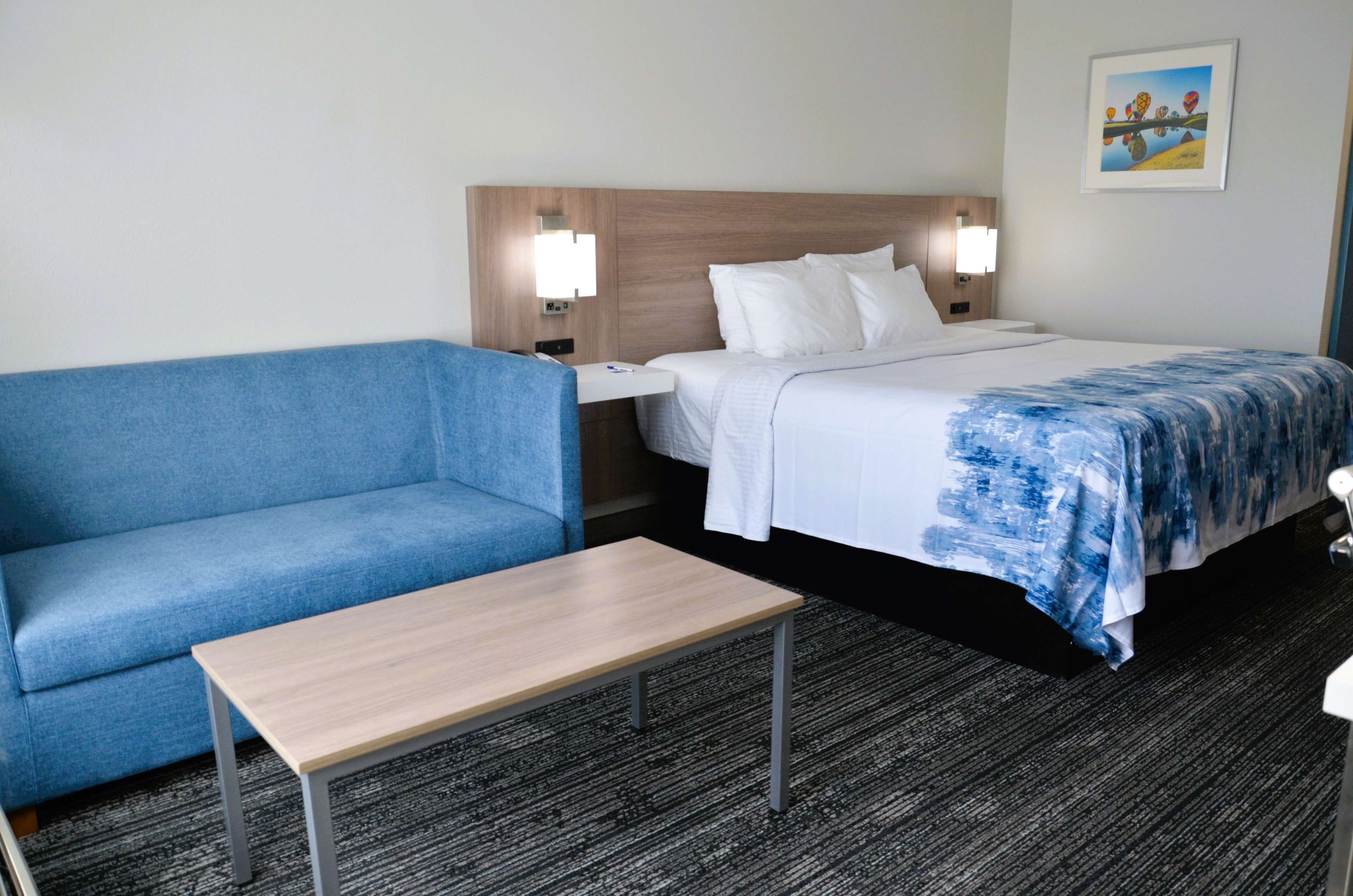 Une chambre d’hôtel avec un lit, un canapé bleu, une table en bois et une table de chevet avec une lampe.
