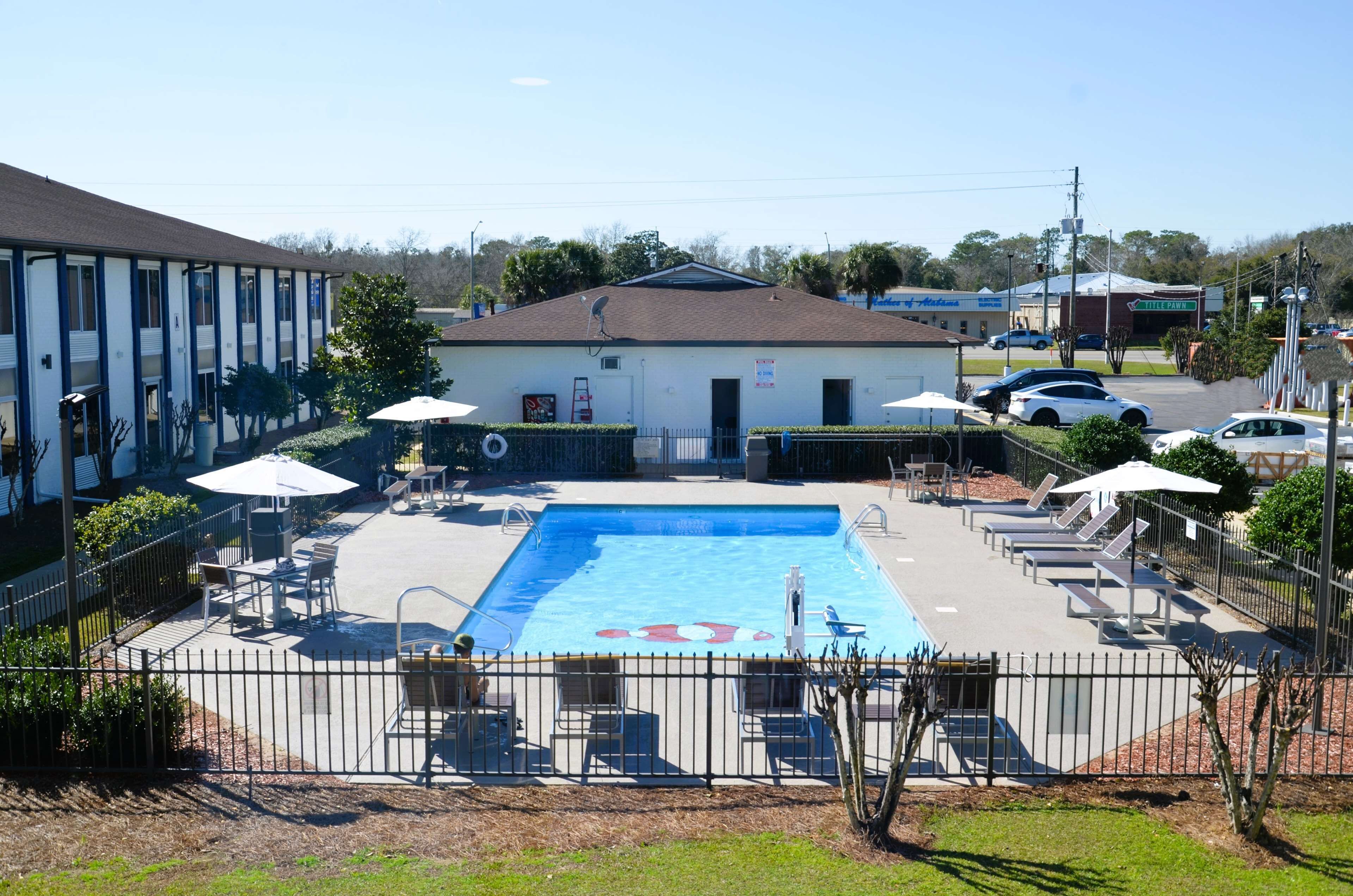 A pool area with lounge chairs, umbrellas, and a building in the background.