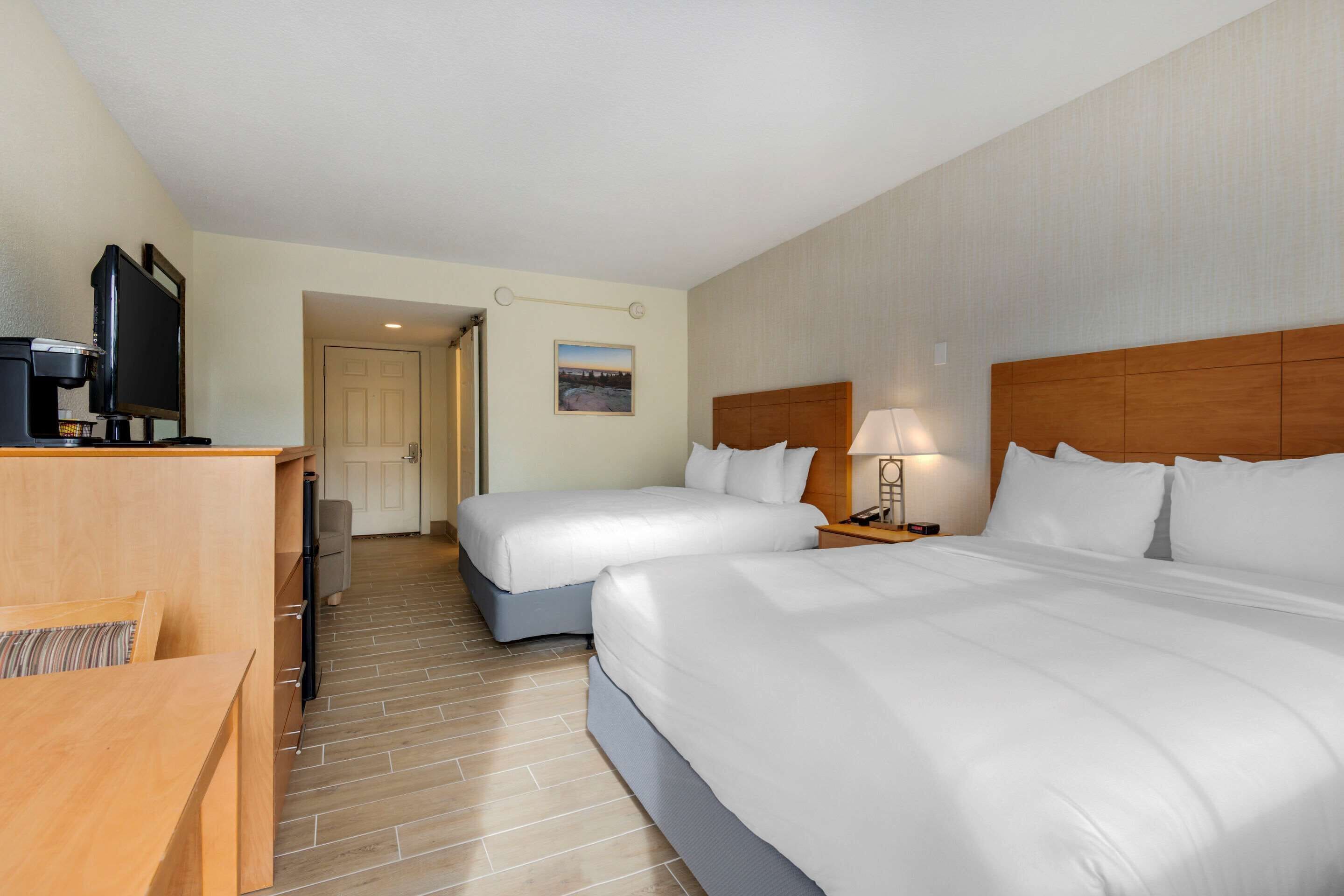 A hotel room with two beds, a desk with a television, and a door leading to another room.