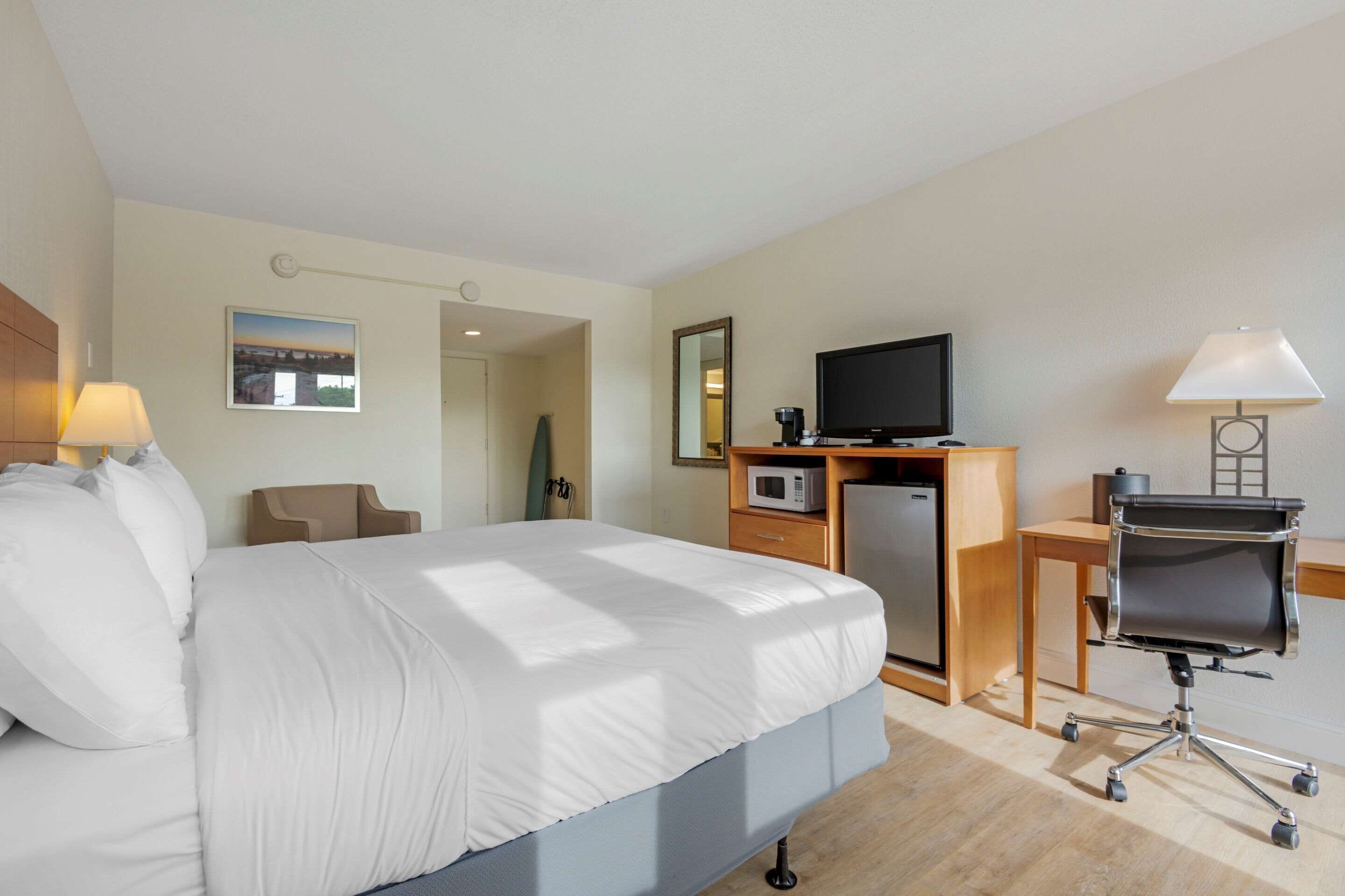 A hotel room with a bed, a desk with a computer, a TV, a microwave, and a chair.
