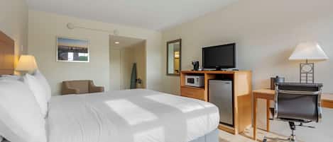 Una camera d'albergo con un letto, una scrivania con un computer, una televisione, un forno a microonde e una sedia.