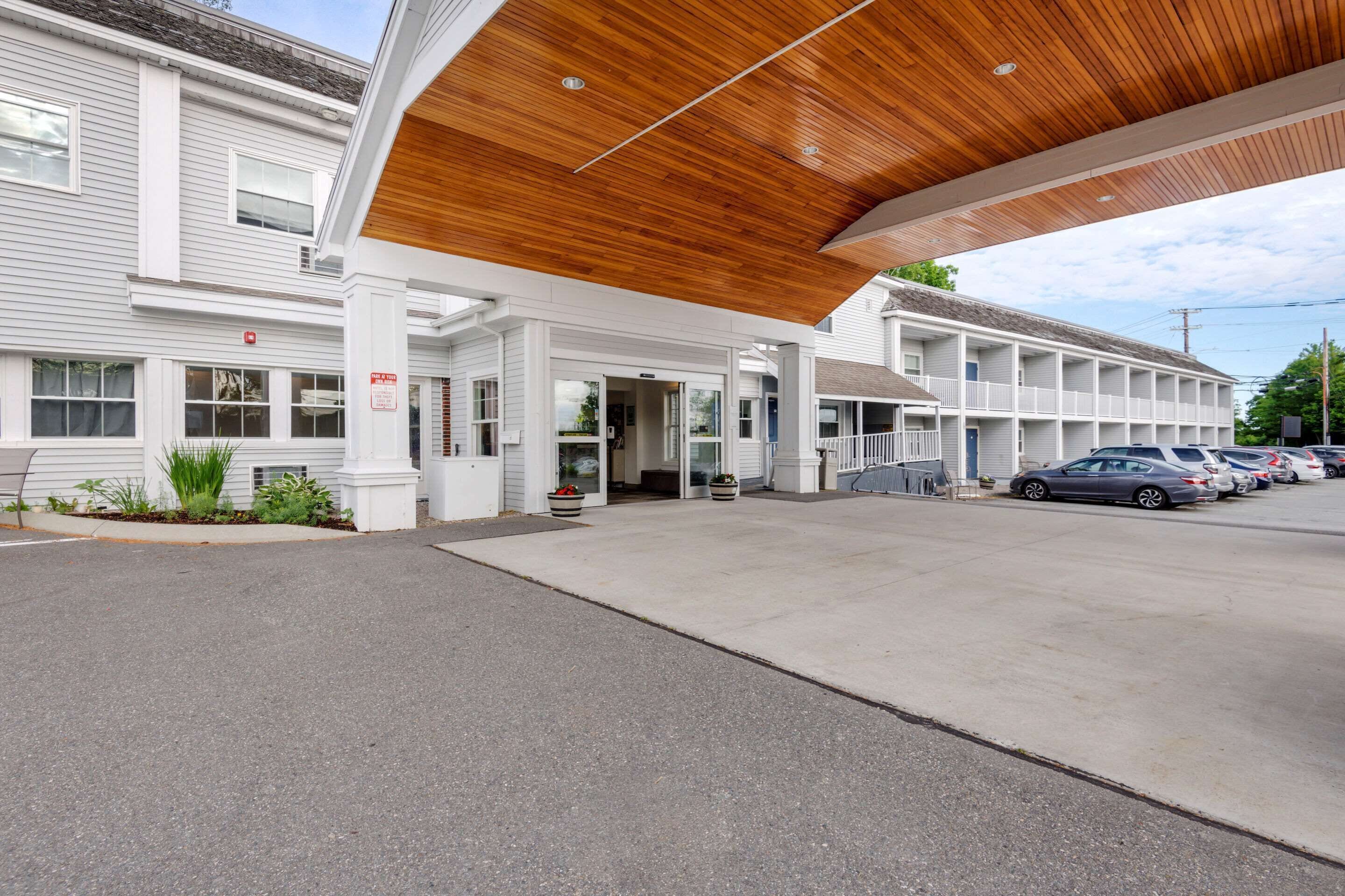 A motel with a covered entrance, a parking lot, and a row of cars parked outside.